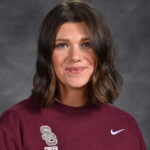A woman with shoulder-length brown hair smiles, wearing a maroon sweatshirt with "Creek Basketball" logo.