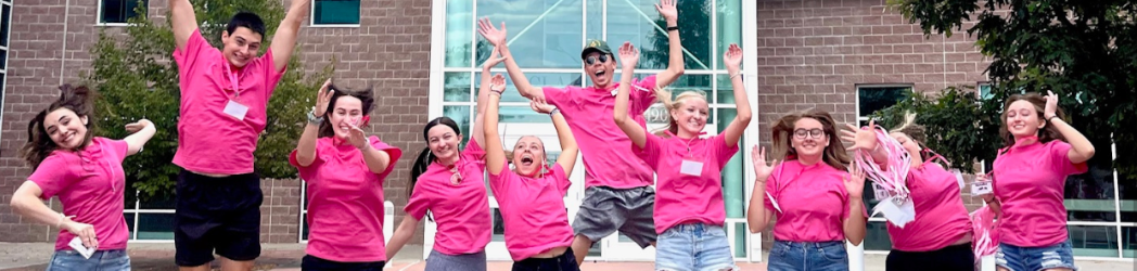 SCLA students in pink shirts jump joyfully in front of Silver Creek High School.
