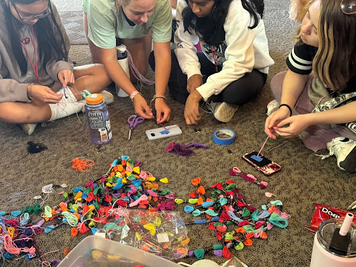 A group of four people sitting on the floor, working on crafts with colorful materials scattered around them.