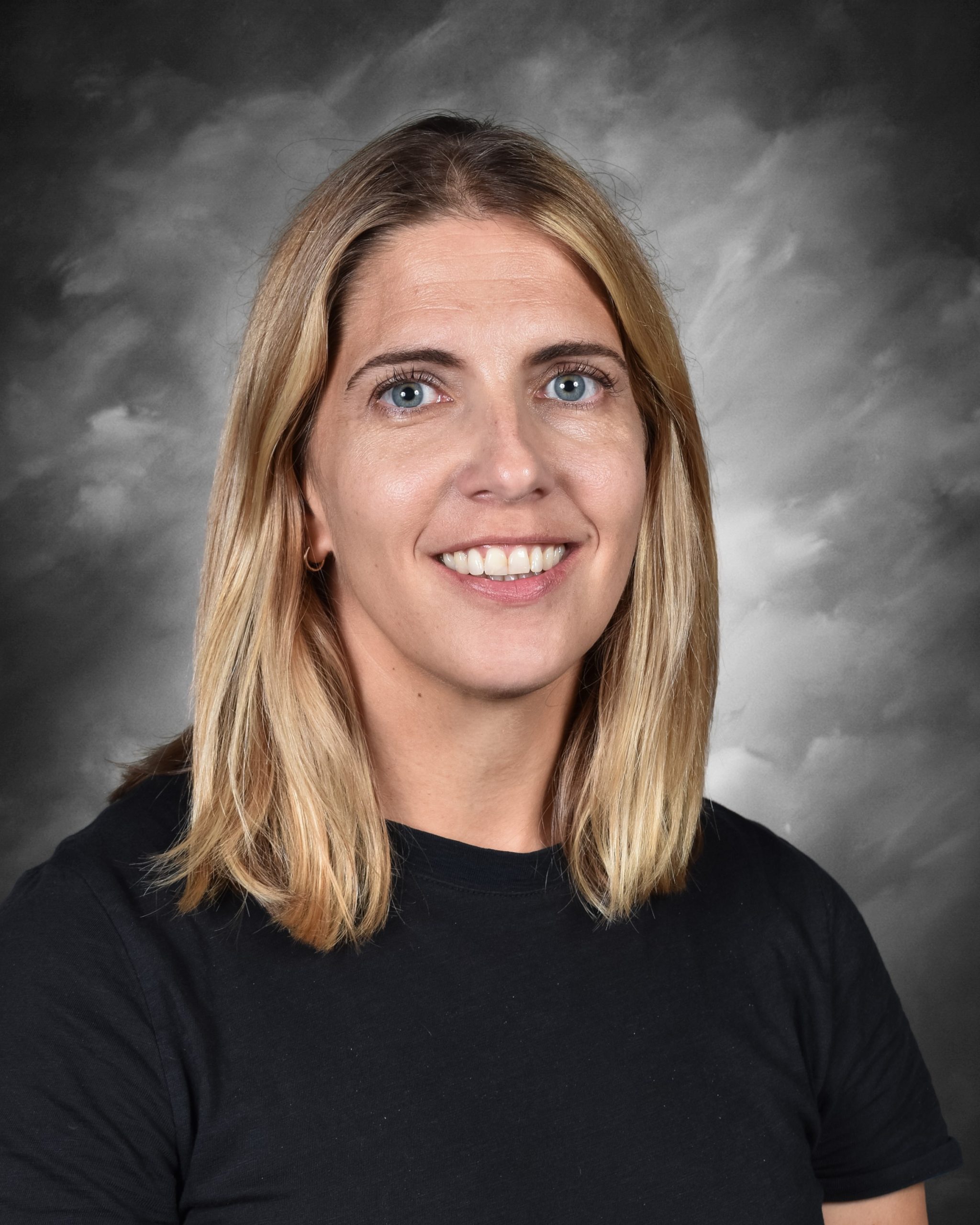 A person with shoulder-length blonde hair smiles against a gray background.